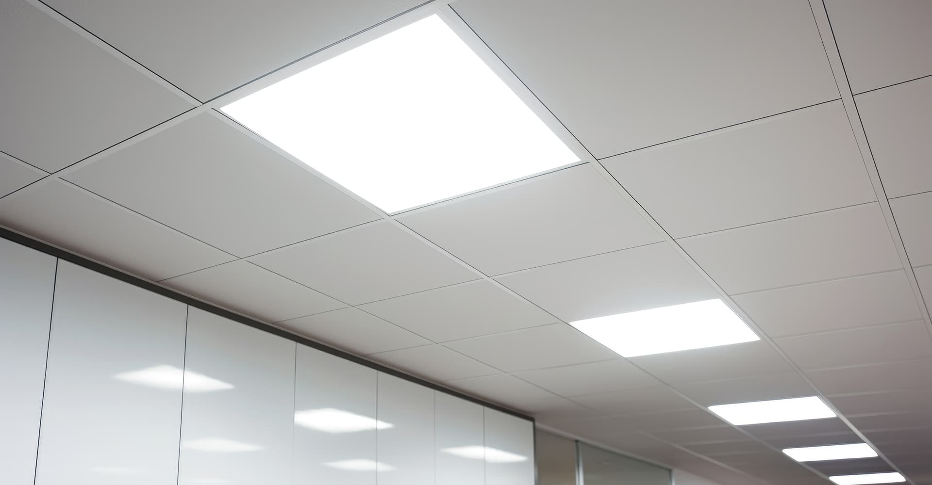 Plafond suspendu blanc avec dalles modulaires et plusieurs luminaires LED rectangulaires encastrés diffusant une lumière vive.