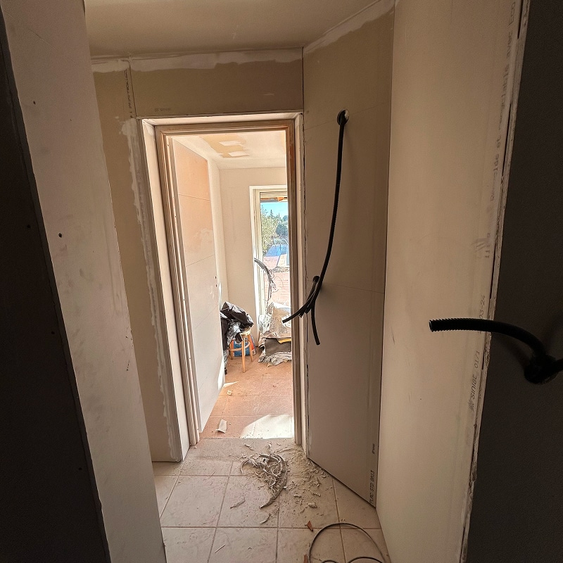 Salon cosy aux murs saumon vue plage Intérieur d'une pièce aux murs saumon clair, avec un canapé clair, un petit frigo et micro-ondes, et une porte-fenêtre donnant sur un extérieur plat et clair.