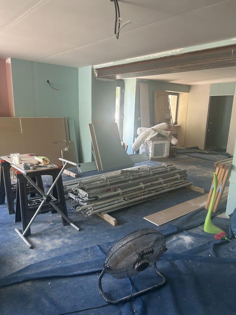 Chantier intérieur : Placo, poutre métal et matériel Chantier intérieur : pose de plaques de plâtre (vert et rose) et poutre métallique, équipement de chantier (scaffalages DAcAMe, tréteaux) et ventilateur.