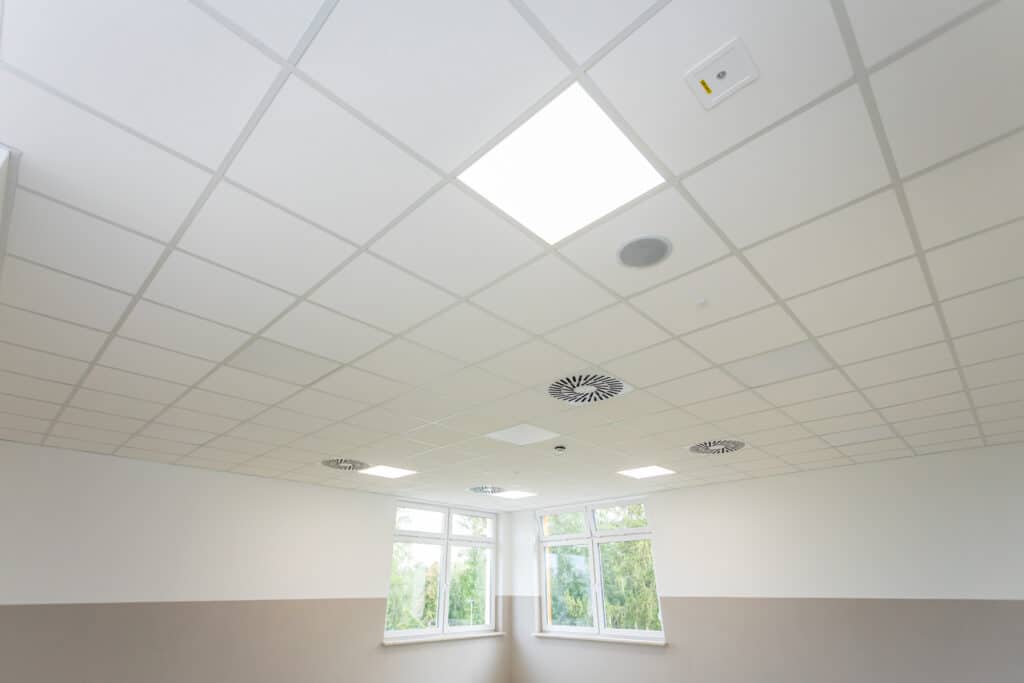 Plafond modulaire blanc avec éclairage et ventilation modernes Plafond blanc à dalles modulaires avec éclairage encastré, diffuseurs d'air circulaires, et un appareil de sécurité étiqueté '10826057'.