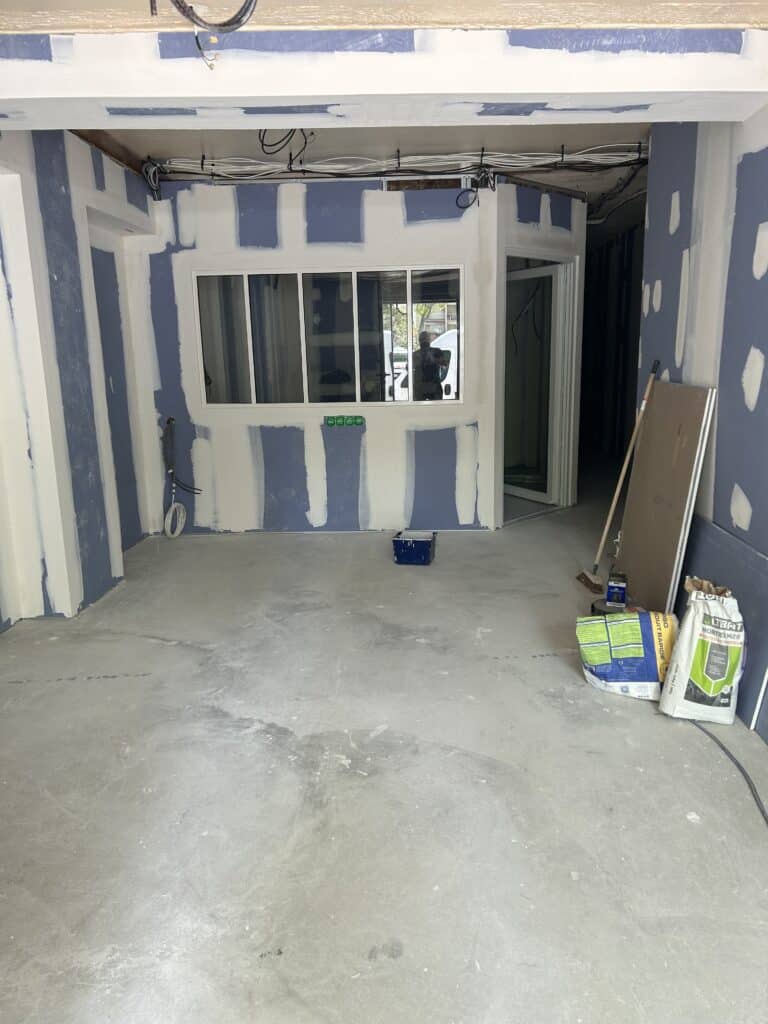 Rénovation Placo : Murs, Fenêtre et Matériaux de Chantier Chantier de rénovation intérieure, murs en plaques de plâtre bleu et enduit blanc, une fenêtre centrale et des sacs de mortier ULTIMAT.