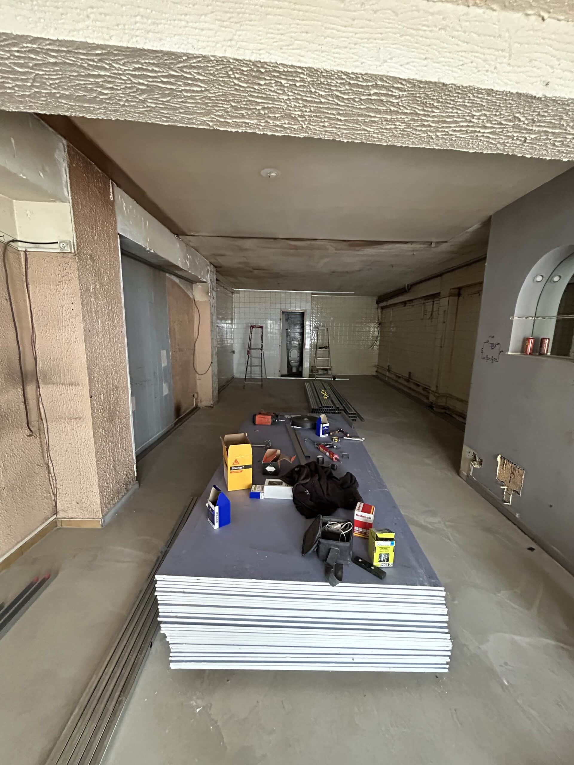 Salon cosy aux murs saumon vue plage Intérieur d'une pièce aux murs saumon clair, avec un canapé clair, un petit frigo et micro-ondes, et une porte-fenêtre donnant sur un extérieur plat et clair.