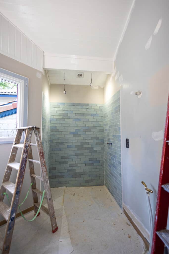 Rénovation Salle de Bain : Carrelage Douche et Chantier Salle de bain en rénovation, douche carrelée bleu-vert et échelle en bois sale sur fond de mur blanc et beige.