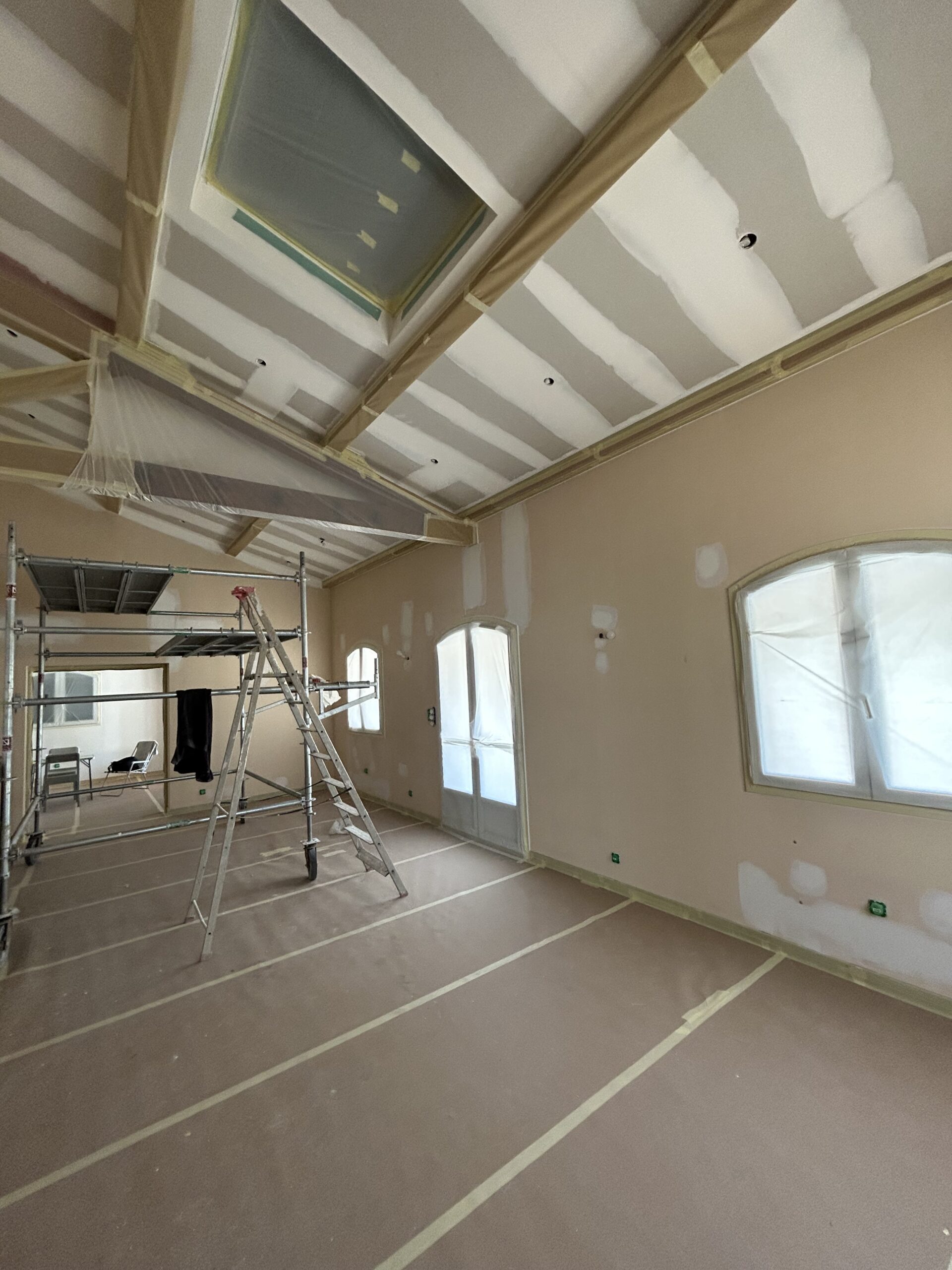 Chantier de Rénovation Intérieure : Préparation Peinture Travaux de rénovation intérieure avec échafaudage, plafond à poutres et fenêtres protégées avant peinture.