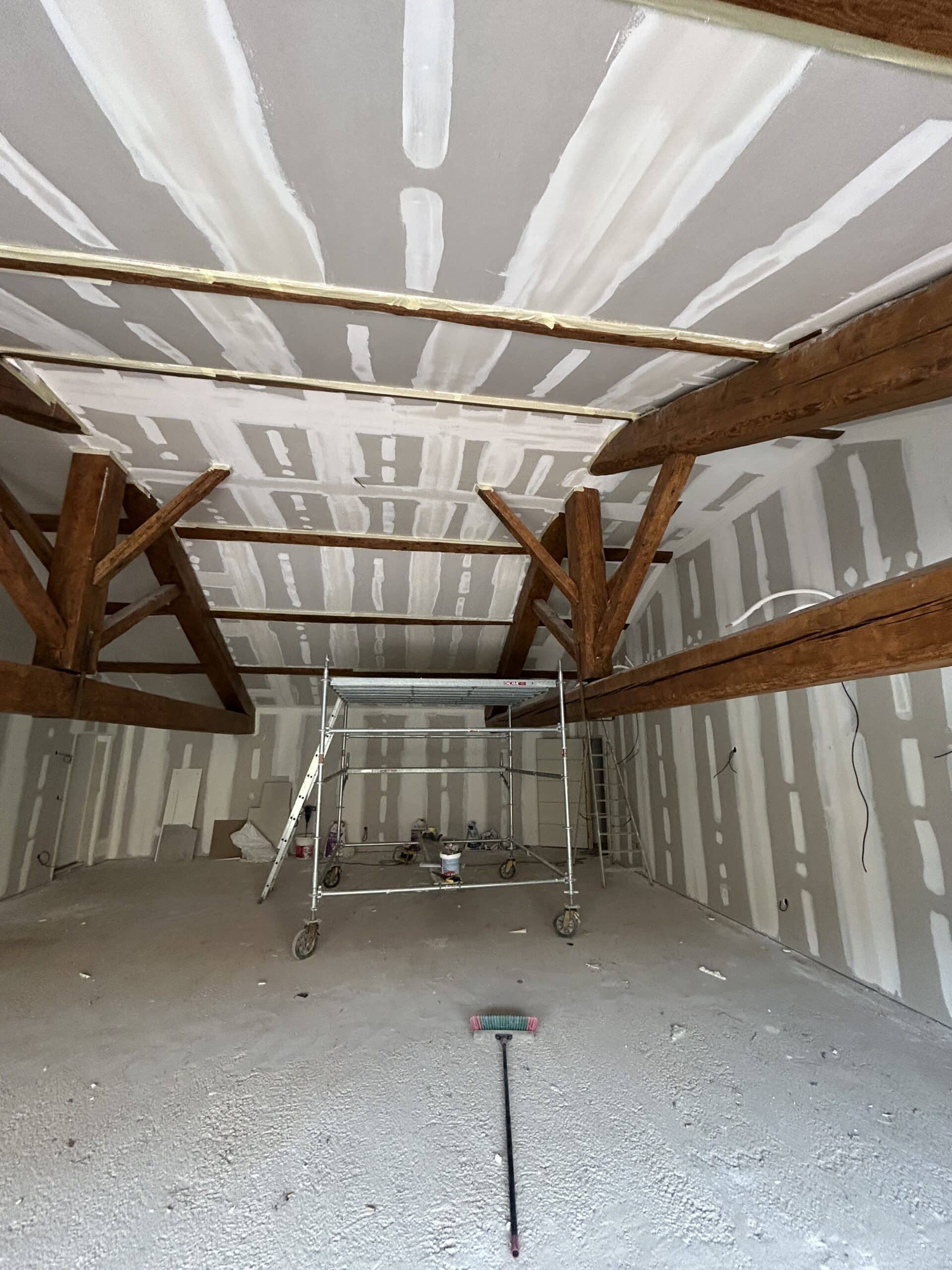 Rénovation : Placo et jointoiement avec poutres apparentes Chantier de rénovation avec plaques de plâtre, jointoiement sur plafond rampant, poutres en bois et échafaudage.